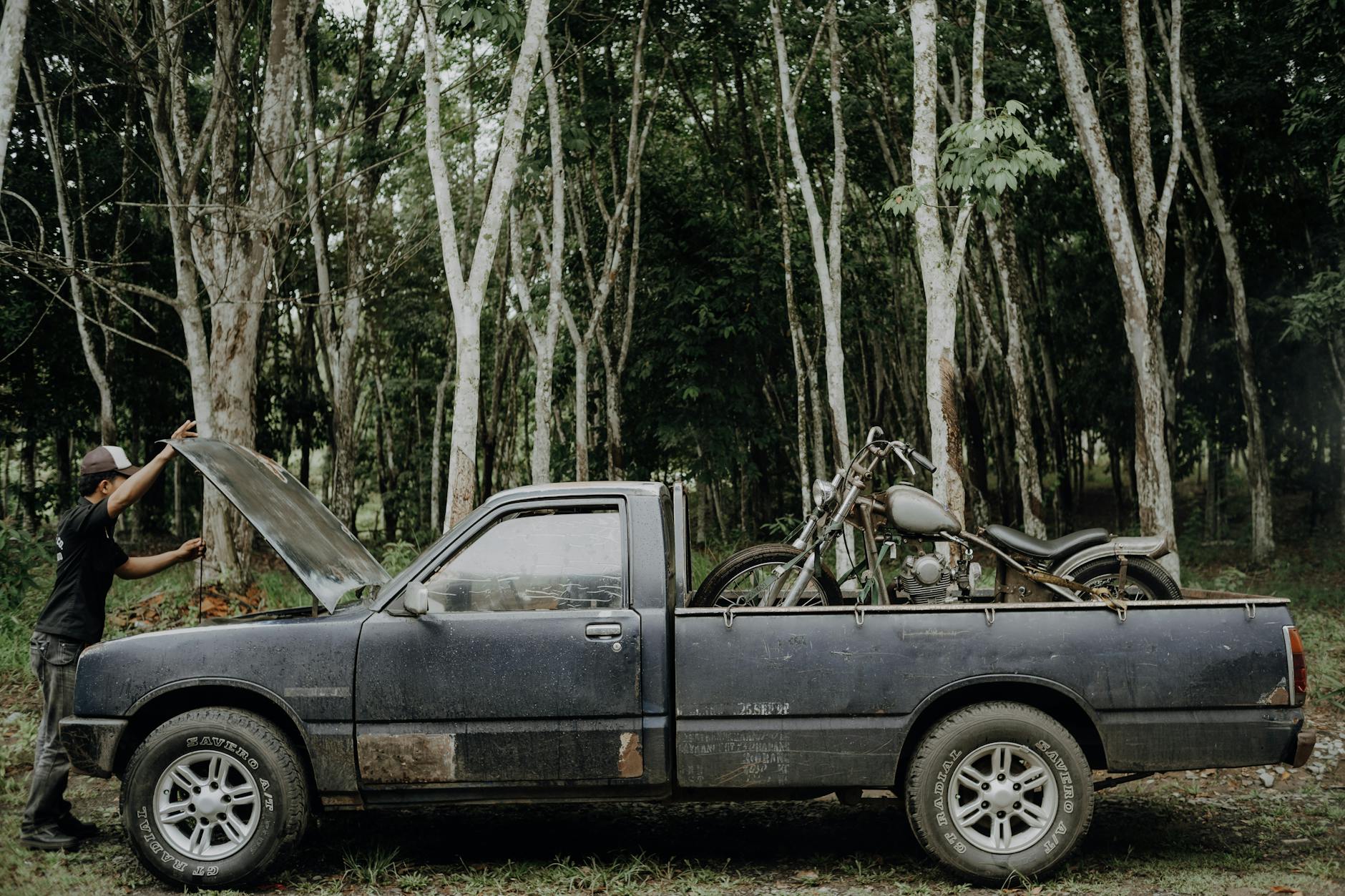 Mężczyzna przy starym pickupie z otwartą maską w tropikalnym lesie