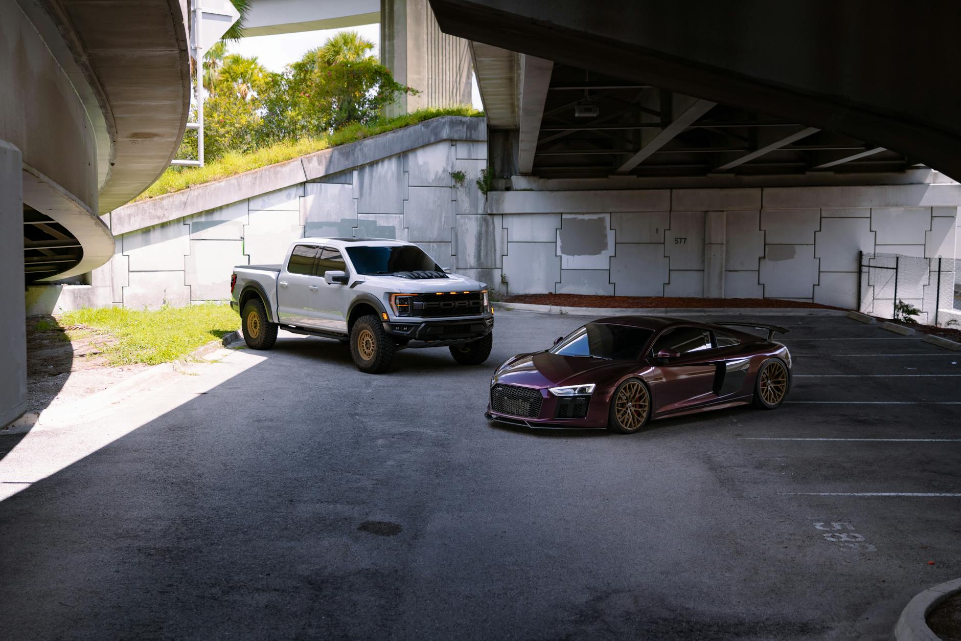 Srebrny pickup i czerwone sportowe auto stojące pod miejską estakadą