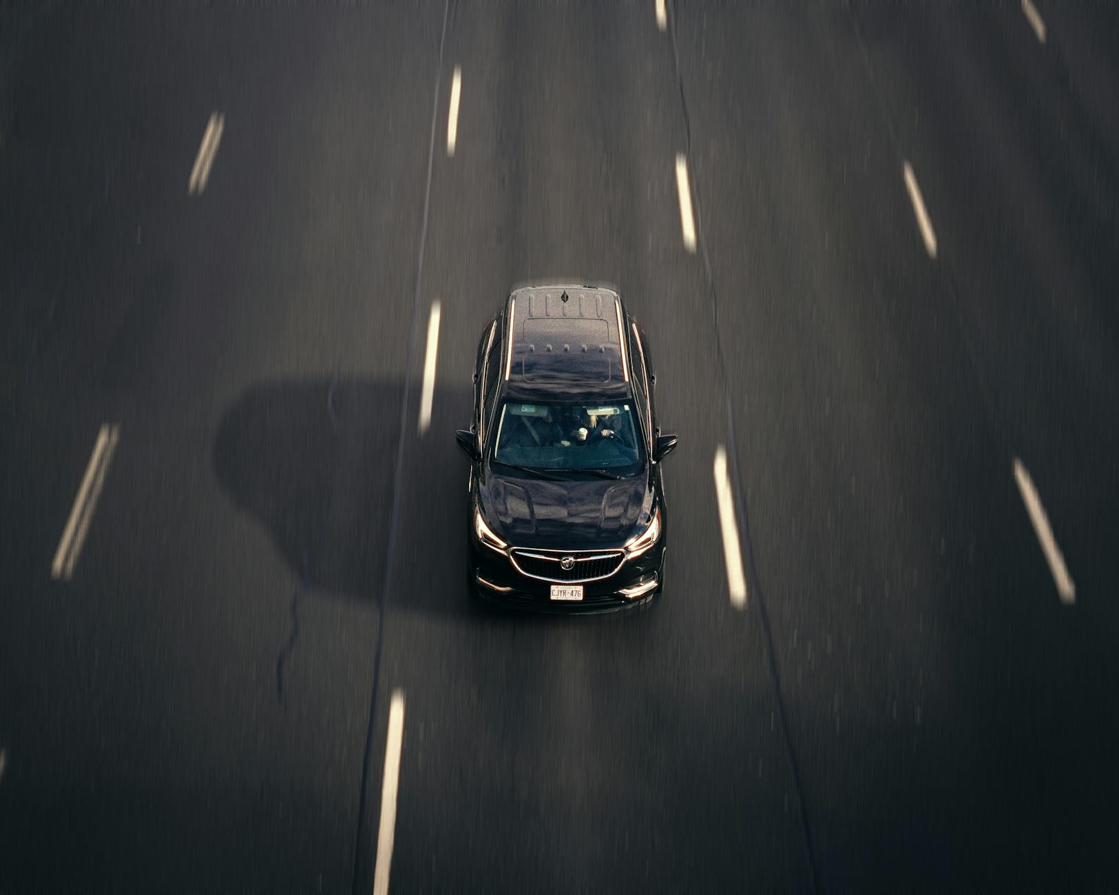 Czarny samochód jedzie autostradą wśród zabudowy dużego miasta