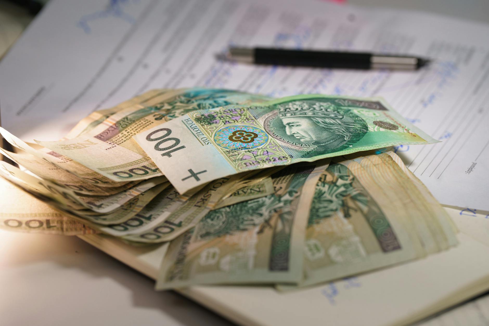 Plik banknotów złotych na dokumentach finansowych z długopisem