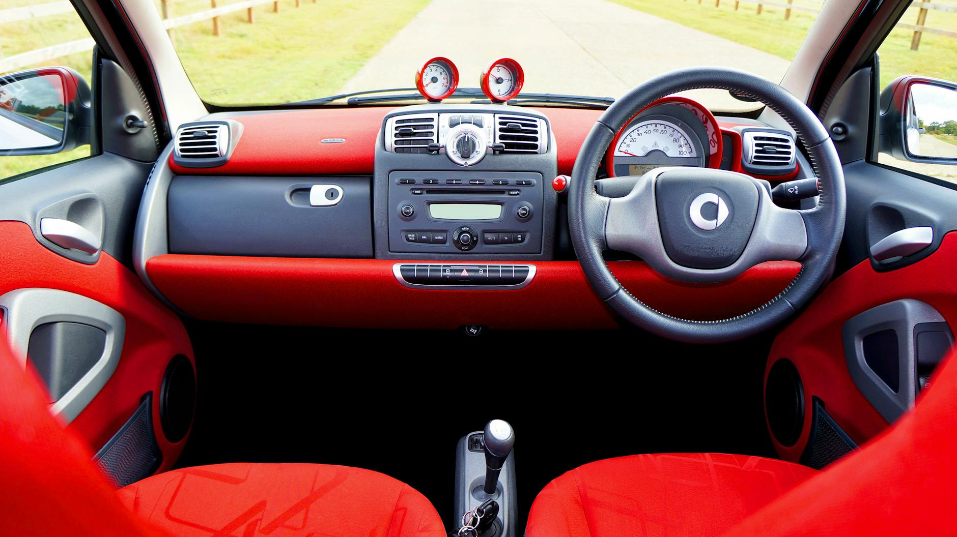 Wnętrze małego czerwonego auta miejskiego, deska rozdzielcza i kierownica