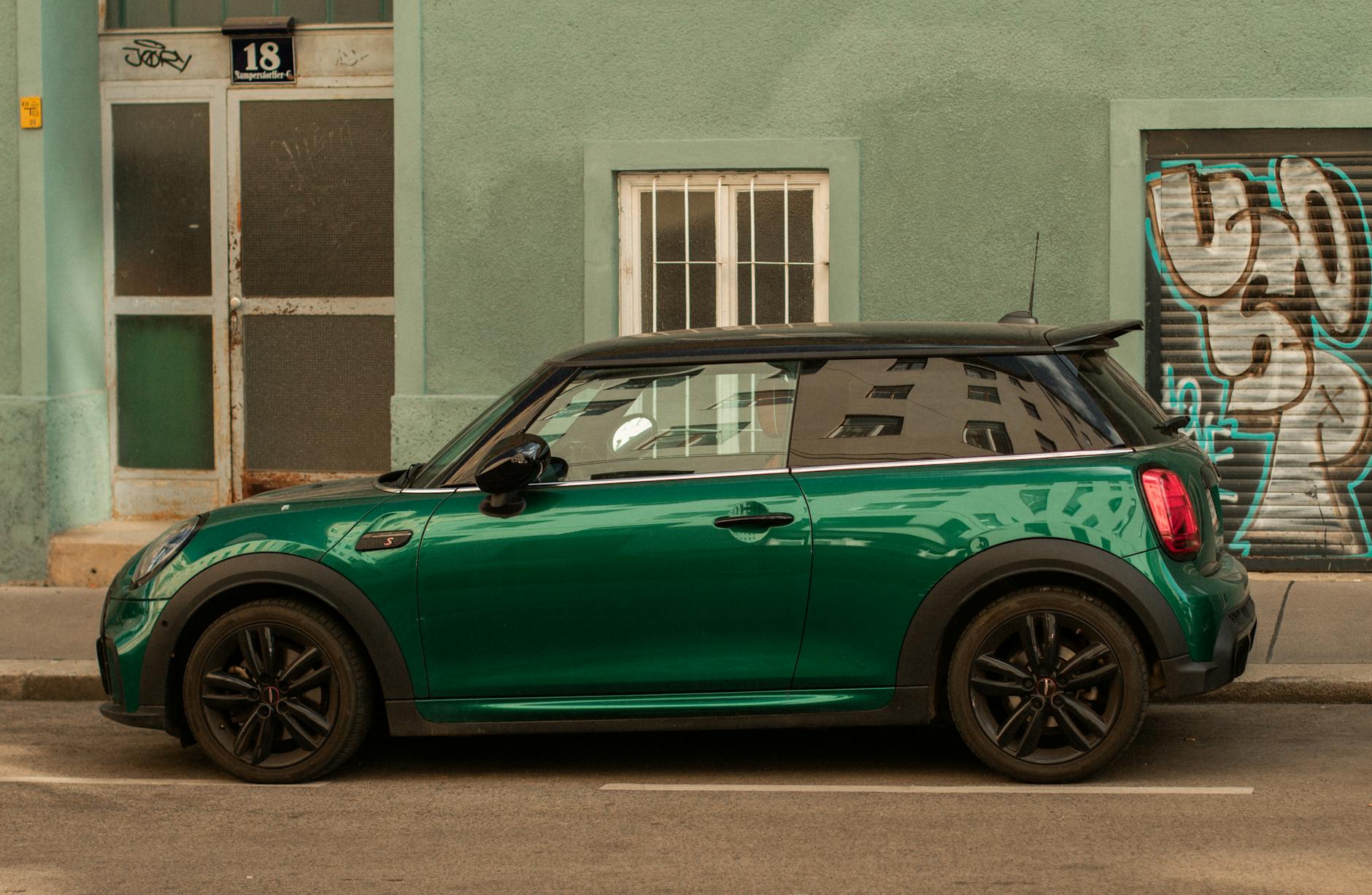 Zielony Fiat 500 z profilu zaparkowany przy ulicy z graffiti