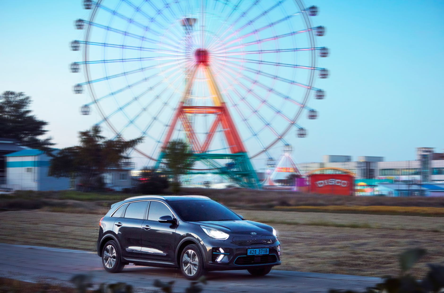 Cadillac Lyriq czy Tesla Model Y który elektryk lepszy dla rodziny Elektryczny SUV przy parku rozrywki z oświetlonym diabelskim młynem