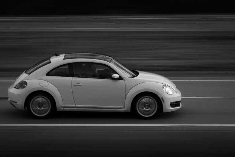 Czarno-białe ujęcie Volkswagena Garbusa jadącego drogą z boku